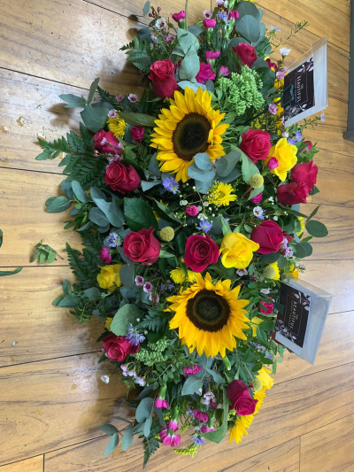 Summer casket tribute - Summer colours casket tribute, with stems such as big headed sunflowers, cerise and yellow roses, spray carnations, waxflower and more.
